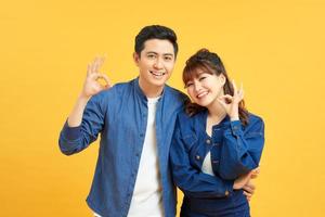 Beautiful young couple together standing over isolated yellow background looking surprised and shocked doing ok approval symbol with fingers. Crazy expression photo