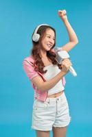 Young happy and excited Asian girl singing online karaoke song with microphone and jumping photo