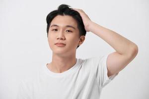 Young handsome man wearing white t-shirt over isolated background Smiling confident touching hair with hand up gesture photo