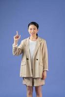 Smiling excited woman showing advertisement, pointing finger up, standing against purple background. photo