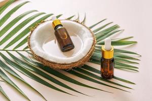 Coconut oil in bottle with open nuts and pulp in jar, green palm leaf background. Natural cosmetic products. photo