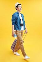 Stylish male tourist in hat carrying suitcase isolated on yellow, travel concept photo