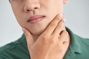 A close up portrait of young thinking man touching his chin with hand and standing against light grey background. Thinking out loud photo