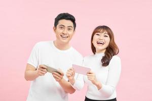 Image of curious man and woman frowning and peeking at each others cell phones, isolated over pink background. photo