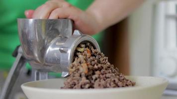 uma mulher incógnita cozinha carne em uma cozinha de casa. carne picada em um moedor de carne mecânico manual. carne cozida fresca é moída em um moedor de carne de metal velho, close-up na cozinha. video