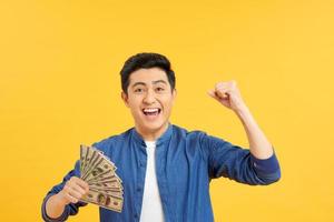 Closeup portrait, happy, excited successful senior lucky elderly man holding money dollar bills in hand isolated yellow background. Positive emotion facial expression feeling. Financial reward savings photo