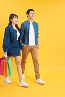 feliz pareja joven caminando con bolsas de compras y mirándose aislado en amarillo foto