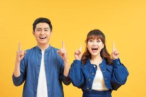 Young beautiful couple standing over isolated yellow background amazed and surprised looking up and pointing with fingers and raised arms. photo