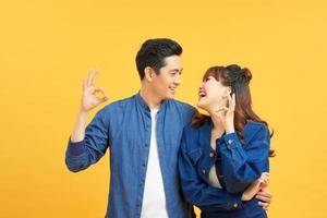 Young beautiful couple standing over isolated yellow background doing ok gesture with hand smiling, with happy face. photo