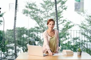 woman in casual clothes checking notes in planner while standing near table in cozy spacious home office photo