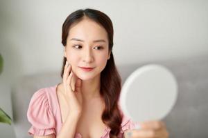 Young Asian woman holding and looking in the mirror at living room photo