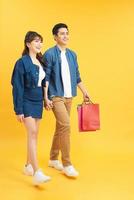 Happy young couple walking with shopping bags and looking at each other isolated on yellow photo