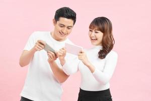 Image of funny young couple man and woman peeking at each others cell phones holding in hands isolated over pink background photo