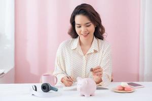 Young Business woman putting coins into piggy bank, writing to report photo