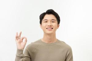 retrato de un joven asiático feliz vestido con una sonrisa informal informal y posando con un signo de mano alegre y okey foto