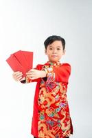 Little Asian boy wearing red traditional Vietnamese suit and holding many of red envelope with smiling face isolated on white background photo