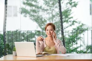 Young businesswoman talking on phone while using laptop at table in office photo