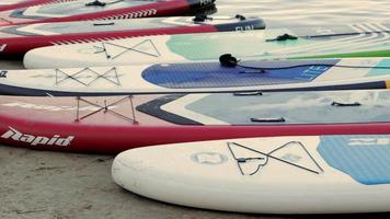 tablas de surf vacías se balancean sobre las olas en un río o lago tranquilo. Deportes acuáticos. muchas tablas en la tienda de alquiler, el sol reflejándose en las ondas del agua. panorámica ucrania, Kyiv - 07 de agosto de 2022.