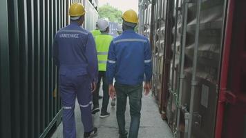 grupo de trabalhadores multirraciais em uniformes de segurança e capacetes de segurança andam e inspecionam o transporte de carga com gerente masculino branco no canto da pilha de contêineres, indústria de transporte logístico de importação e exportação de mercadorias. video