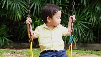 un niño está felizmente sentado en un columpio en el patio de recreo video