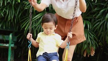 un niño está felizmente sentado en un columpio en el patio de recreo video