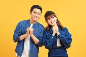 Young couple posing in a yellow background clasping hands at camera in congratulations gesture. photo