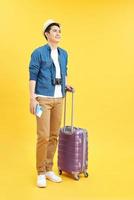 Full length side portrait of happy asian male traveler walking with suitcase against isolated yellow background photo