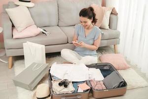 mujer empacando maleta, preparándose para viajar y hablando por móvil. concepto de preparación de maleta de viaje foto