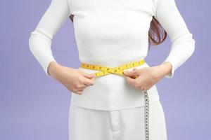 Photo of a fit and healthy young lady measuring her waist with a tape measure in centimeters and millimeters.