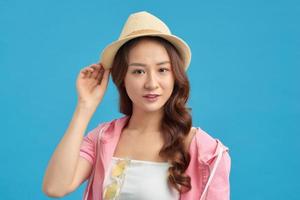 Beautiful young woman wearing summer straw hat posing against blue background photo