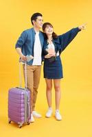 Portrait of a young beautiful couple with suitcase and looking up. Travel concept. Isolated yellow background. photo