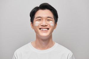 grooming, skin care and people concept - smiling young indian man applying cream to face over white background photo