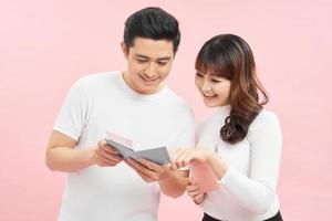 happy asian man and woman holding passports and air tickets while looking at camera isolated on pink photo