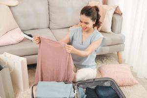 Young asian woman packing clothes into travel bag - Luggage and people concept photo