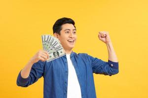 Closeup portrait, happy, excited successful senior lucky elderly man holding money dollar bills in hand isolated yellow background. Positive emotion facial expression feeling. Financial reward savings photo