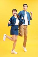 Full length portrait of amazed couple man and woman in basic t-shirts rejoicing while clenching fists isolated over yellow background photo