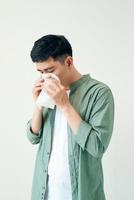 joven enfermo guapo y estornudo aislado en el fondo de la pared blanca. concepto de enfermo. gente asiática. foto