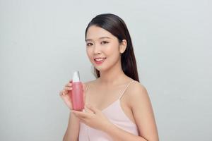 Portrait of a young woman holding pink bottles with lotion on white background photo