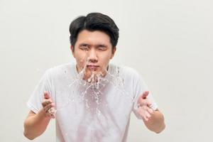 un hombre guapo se está lavando, salpicando agua, en un fondo blanco foto