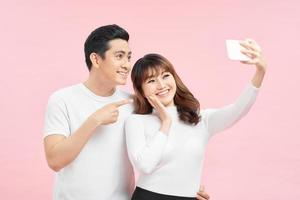 Close up portrait of young asian, attractive, lovely, smiling, mature couple making selfie on mobile phone over pink background photo