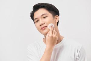 Facial care. Portrait of a positive delighted nice man holding a cotton pad and using it while caring about his face photo