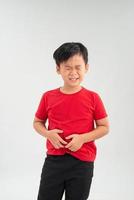 Sad little Asian boy suffering from stomach ache, holding his stomach, isolated on white background. photo