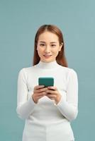 Smiling lovely young woman standing and using cell phone over violet background photo