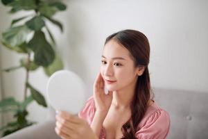 Young Asian woman holding and looking in the mirror at living room photo