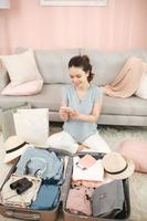 Upper view of smiling elegant woman at modern home in sunny summer day using mobile travel agent app on smartphone near open travel suitcase. photo