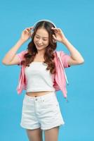 Cheerful young asian woman girl posing isolated on blue wall background. Listen music with headphones, dancing photo