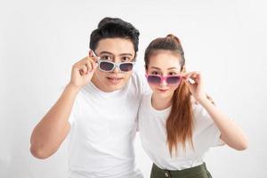 Beautiful cute adorable surprised couple putting colorful spectacles down showing wow emotion over yellow background, isolated photo