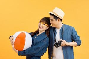 Playful Asian couple in summer casual clothes with beach accessories studio shot isolated on yellow background photo