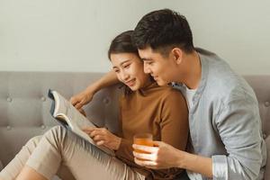 A young, attractive couple is seated together on a couch and are reading a tablet together. photo