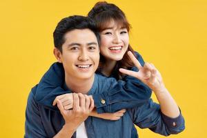 Portrait of happy couple man and woman in basic t-shirts showing peace sign together while doing piggyback ride isolated over yellow background photo